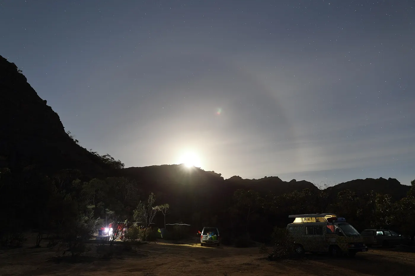 A campground at night with the moon rising over a dark ridge