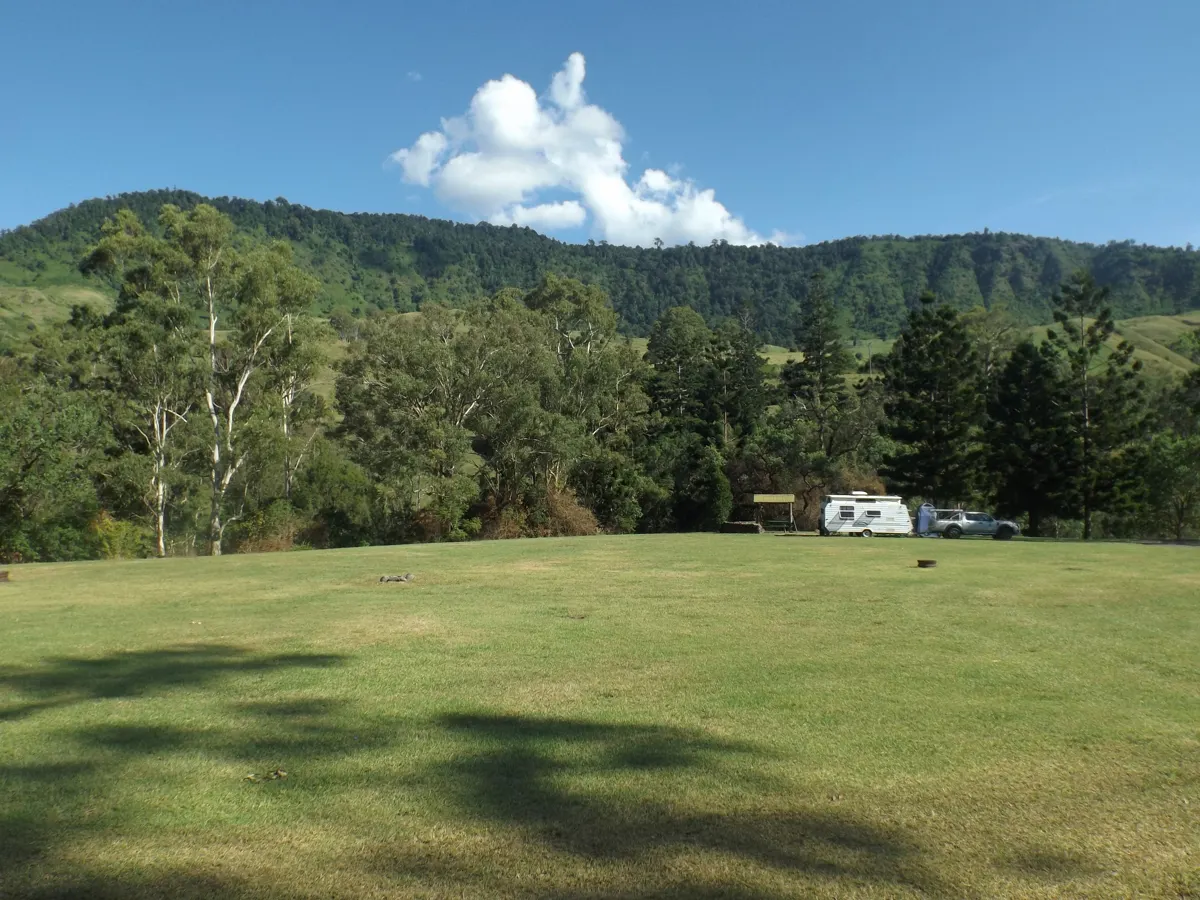 A caravan parked on a grassy campground beneath the McPherson Range, Queensland